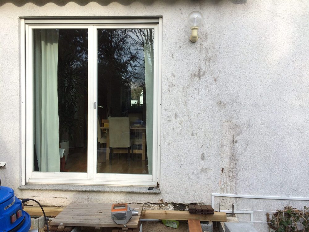 Hausfassade mit dunklen Efeuresten und Haftwurzeln auf dem Putz vor der Reinigung