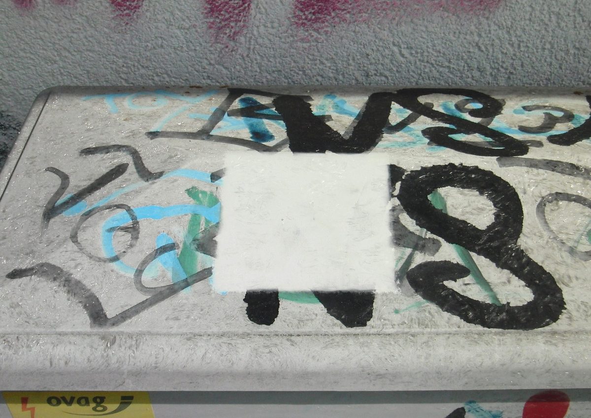 Probefläche auf einer besprühten Betonbrüstung: das freigelegte helle Rechteck zeigt den Untergrund nach der Behandlung, ringsum liegt das Graffiti noch