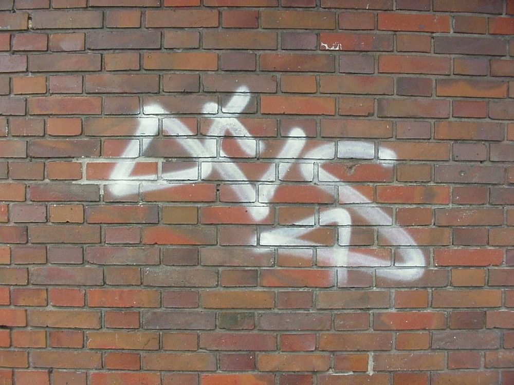 Klinkerfassade mit weißem Graffiti-Schriftzug vor der Reinigung