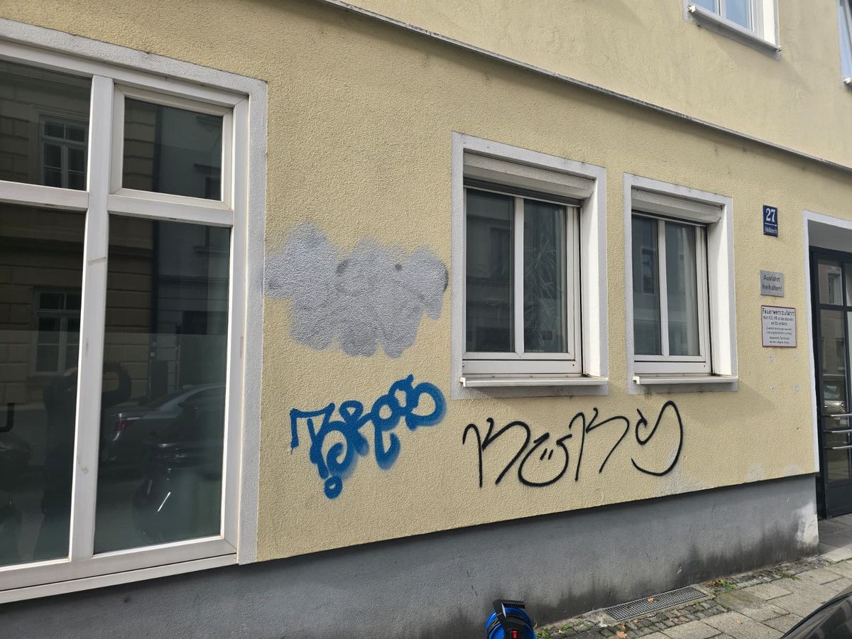 Blauer Tag auf einer beigen Putzfassade neben einem grauen Übermalungsfleck