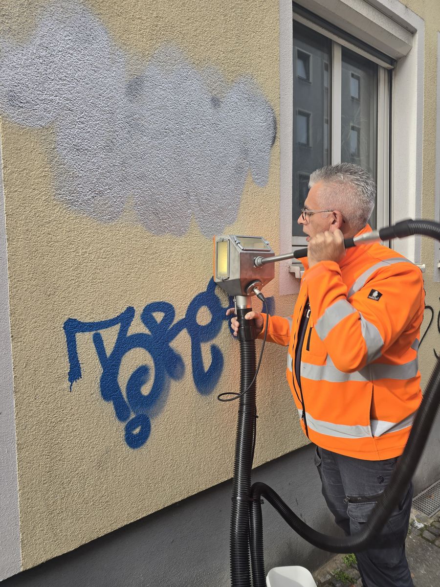 Mitarbeiter in Warnweste entfernt einen blauen Tag von einer Putzfassade, die gereinigte Fläche ist bereits sichtbar