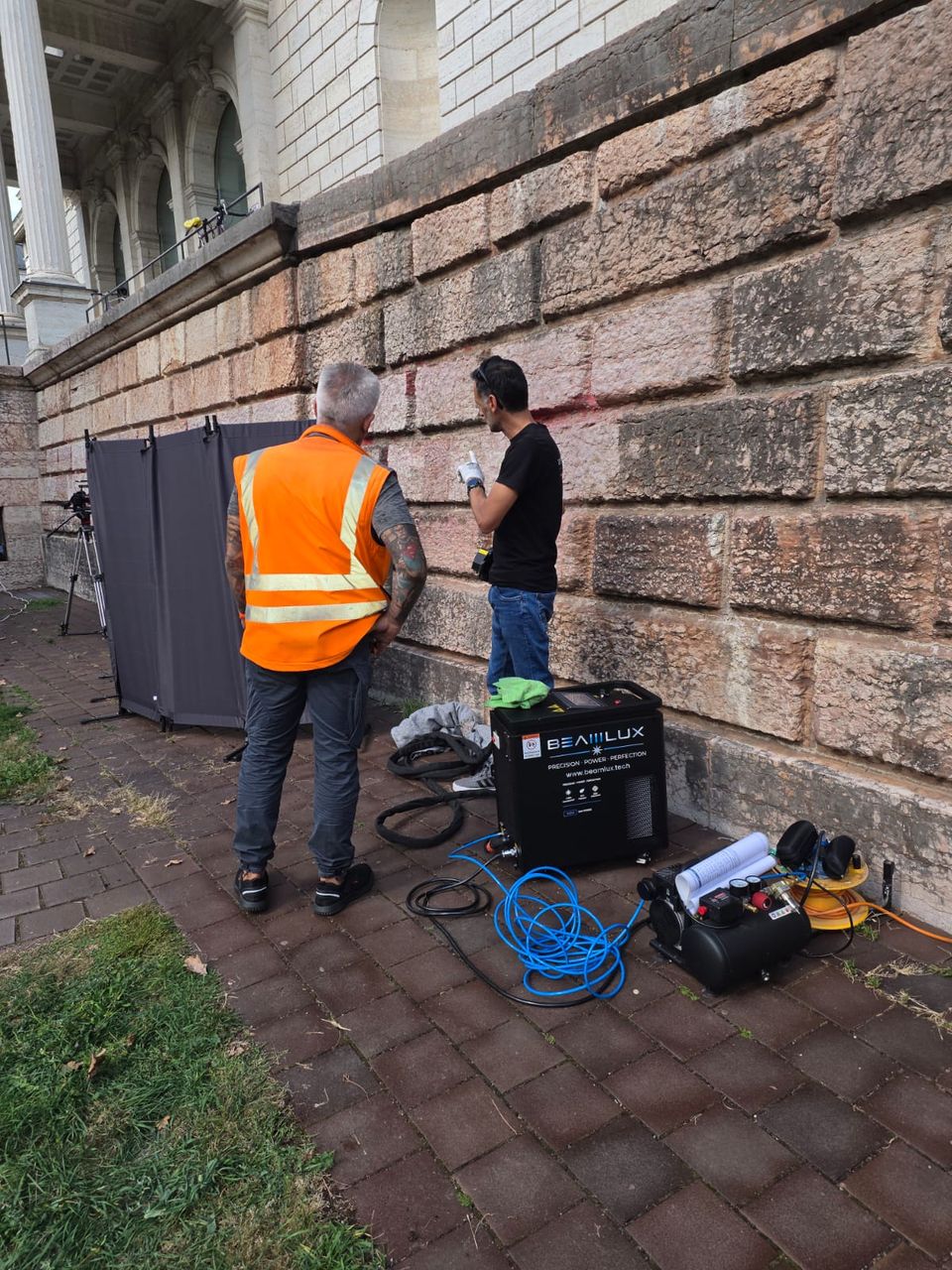 Laserreinigung an einer Sandsteinmauer in München: Beamlux-Lasergerät, Druckluft und Schutzwand vor Ort